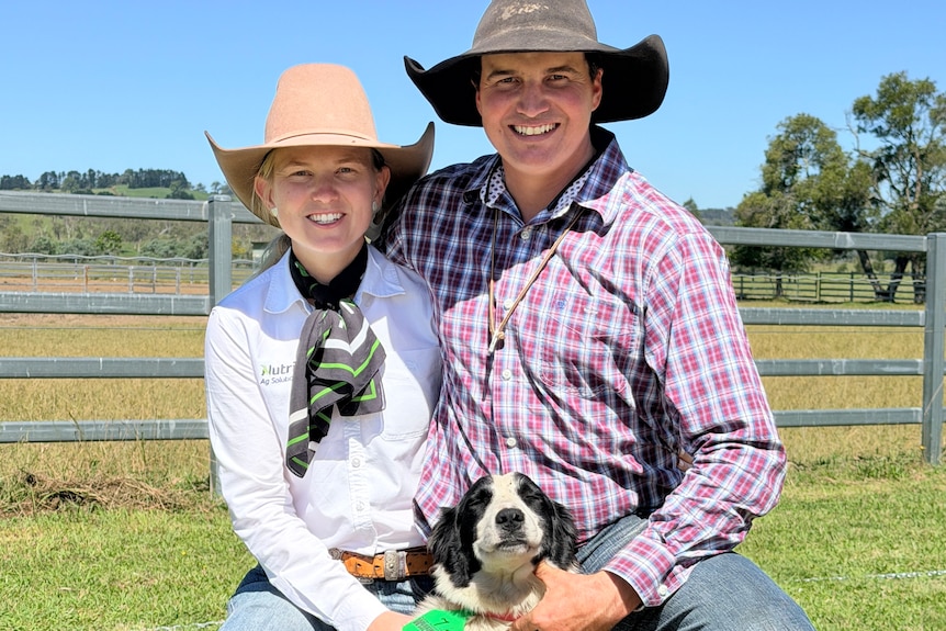 A man and a woman smile at the camera kneeling with a black and white dog.