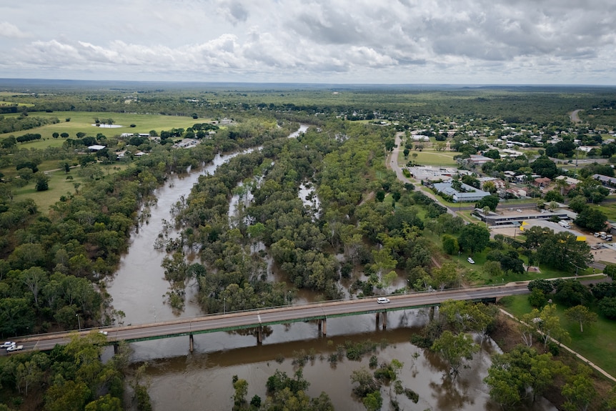 Aerial photo of a flooded river flowing beneath a bridge.