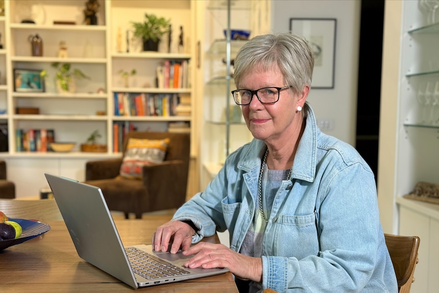 An older woman with short blonde hair sitting in front of a laptop.