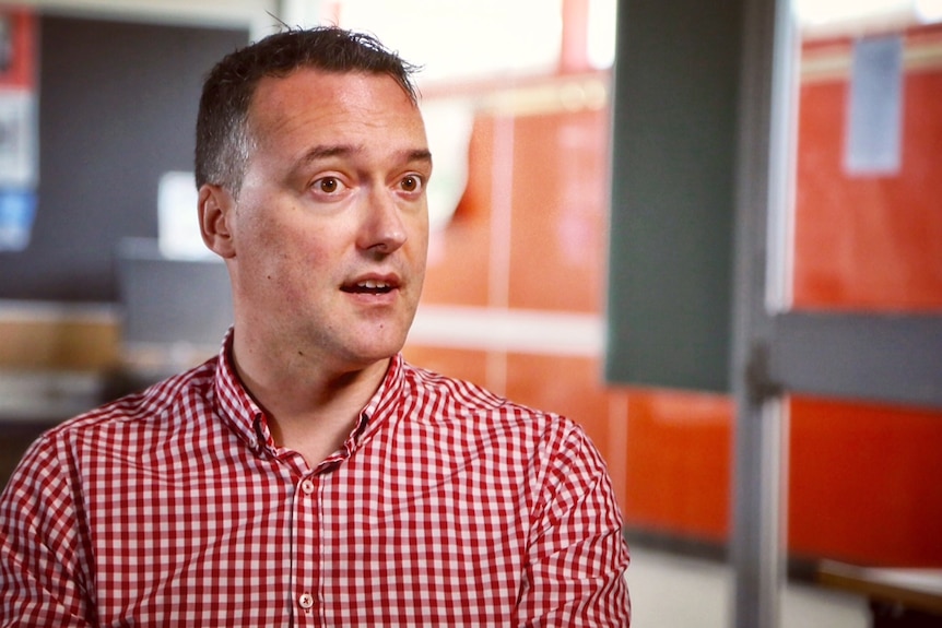 A man is interviewed. He is wearing a checkered shirt.
