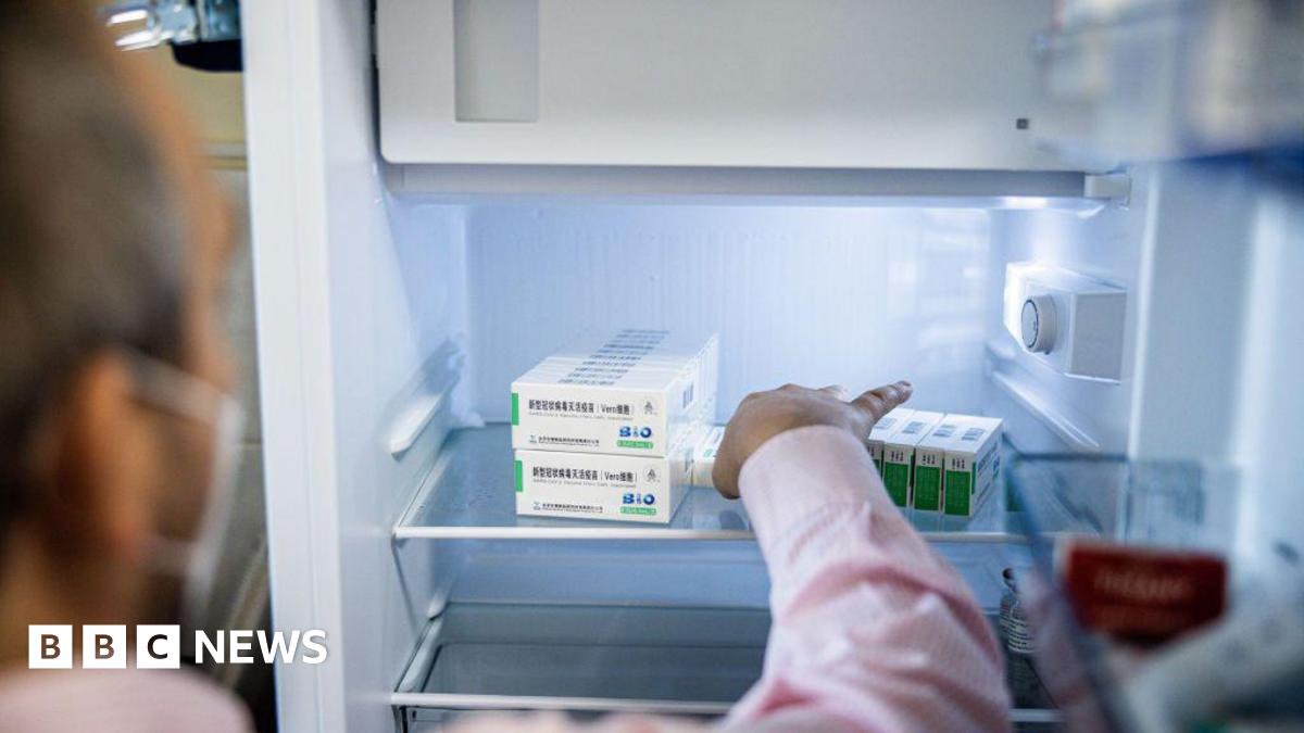 A woman with dark hair and a multiple colour jumper siting on a green sofa inside her living room.