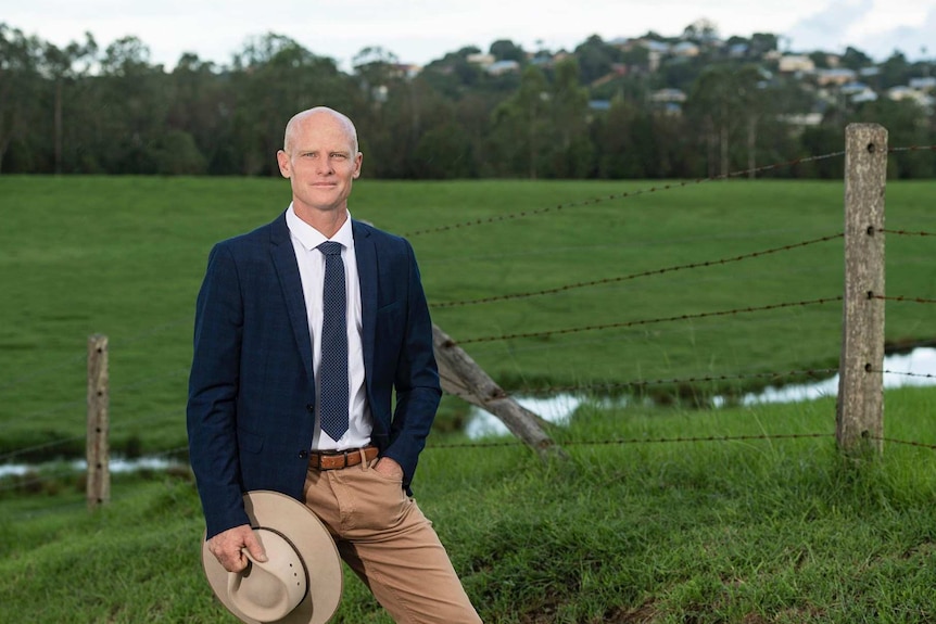 Man standing in field wearing a suit and tie, in front of a fence