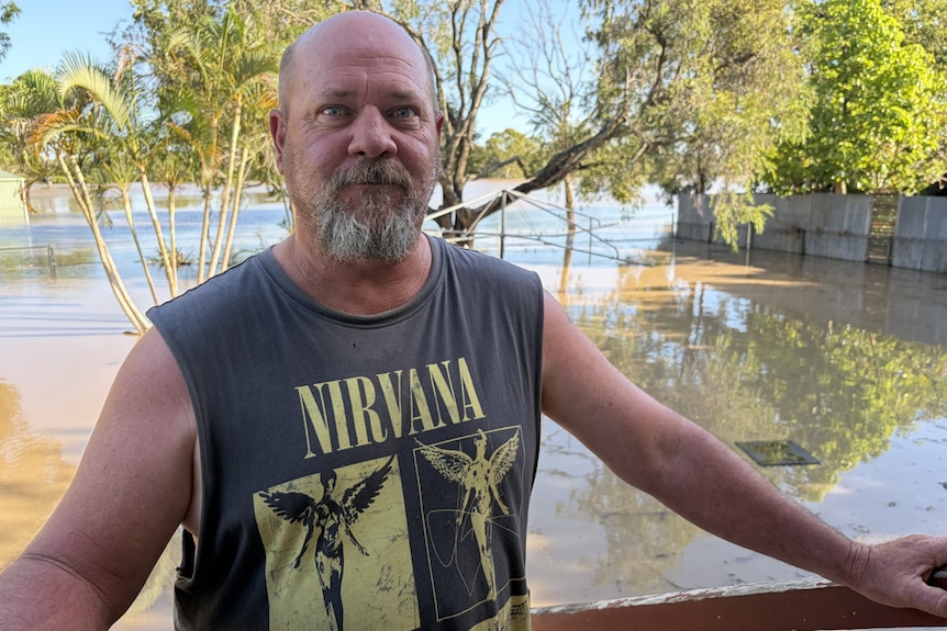 man in singlet staring forward with floodwaters in background in backyard