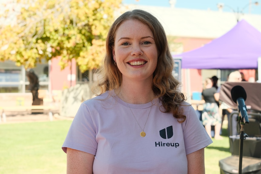 Image of Olivia Nolan who has long curly hair and smiles at the camera standing outside.