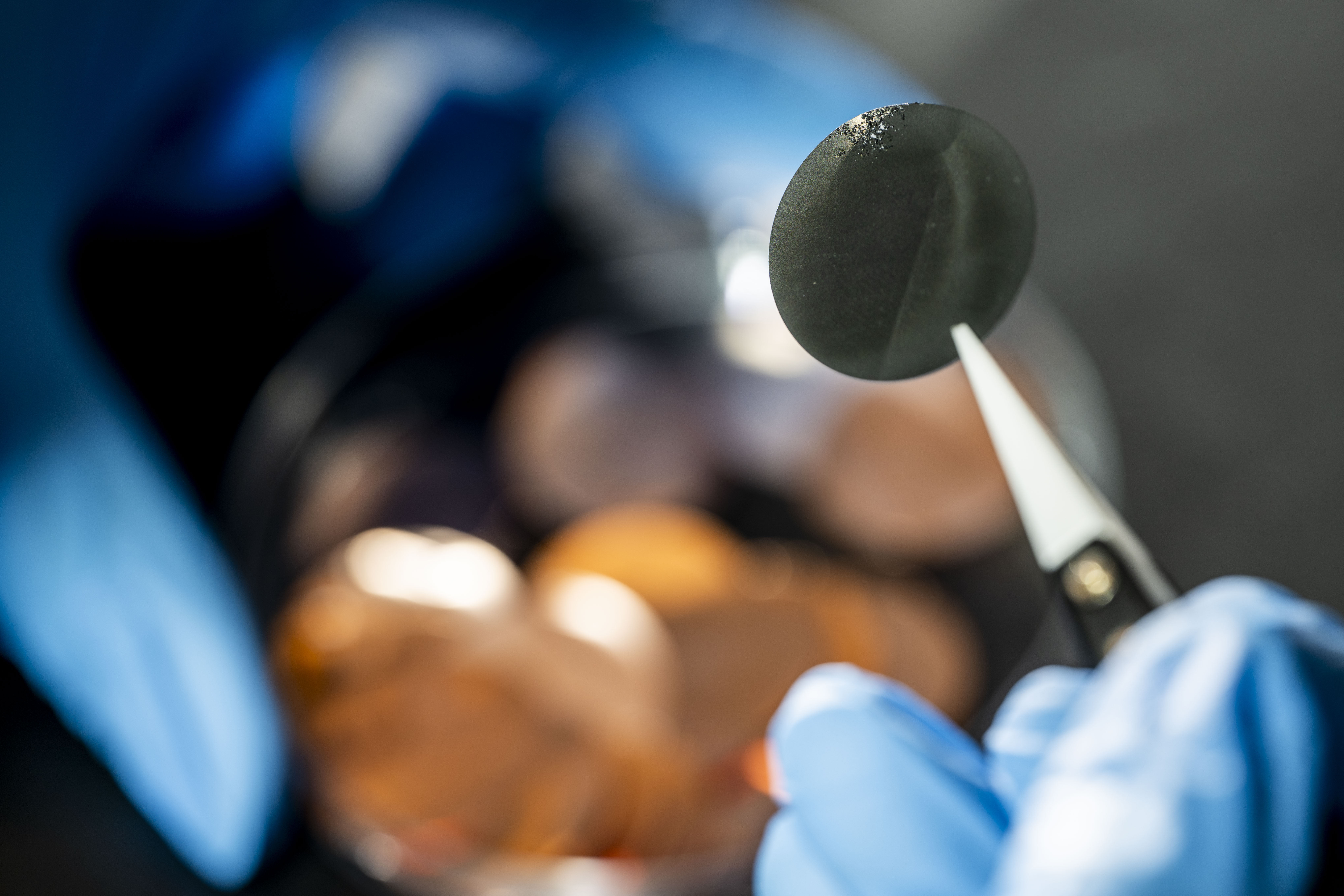 Close-up of gloved hands handling materials in a laboratory, part of electric vehicle battery research.