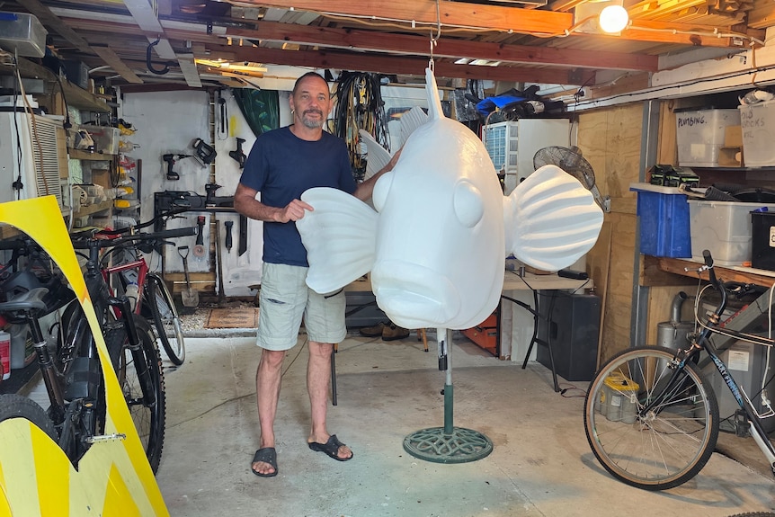 Man with a giant fibreglass fish in his shed.
