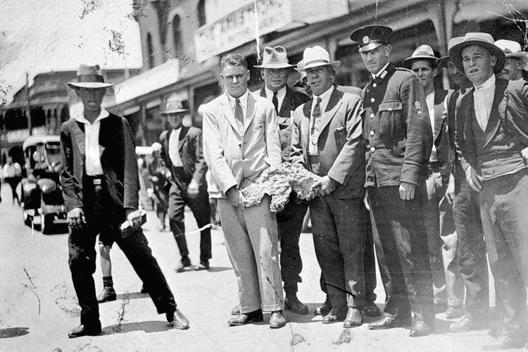 Men wearing suits holding a large gold nugget in an old black and white photograph.