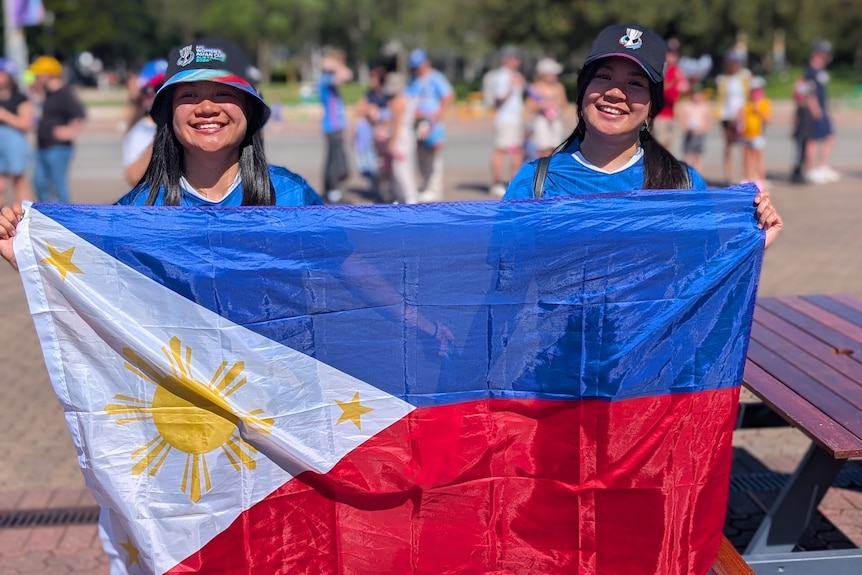 Two women smile and hold a Philippines flag.