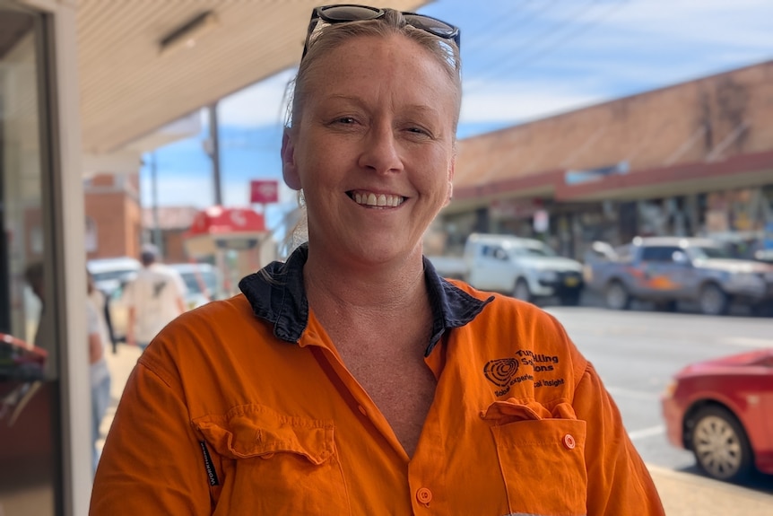 Woman on town footpath, wearing orange work safety shirt and sunglasses on top of her head