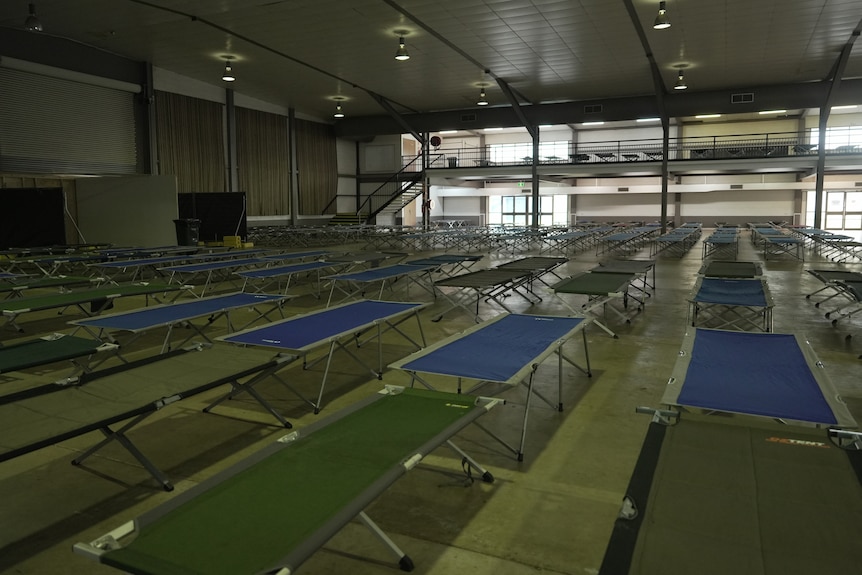 Rows of temporary beds lined up inside a large empty building.
