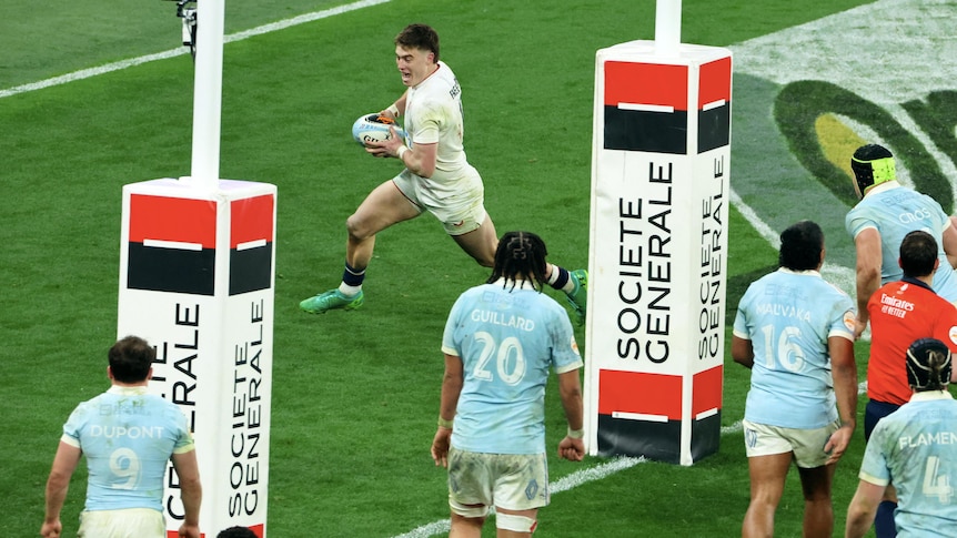 An excited English rugby union international runs behind the posts to score a try as the French defence watches.