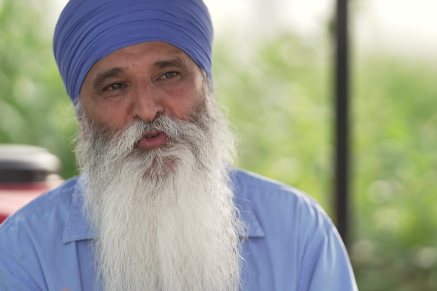 A Sikh man talking to the camera with blurry greenery behind him.