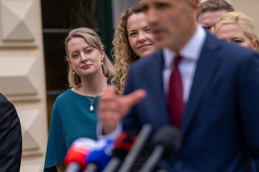 A woman wearing a green shirt smiles towards a man speaking into a microphone.