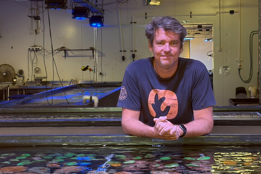 A man standing behind an aquaculture tank in a large shed filled with tanks.