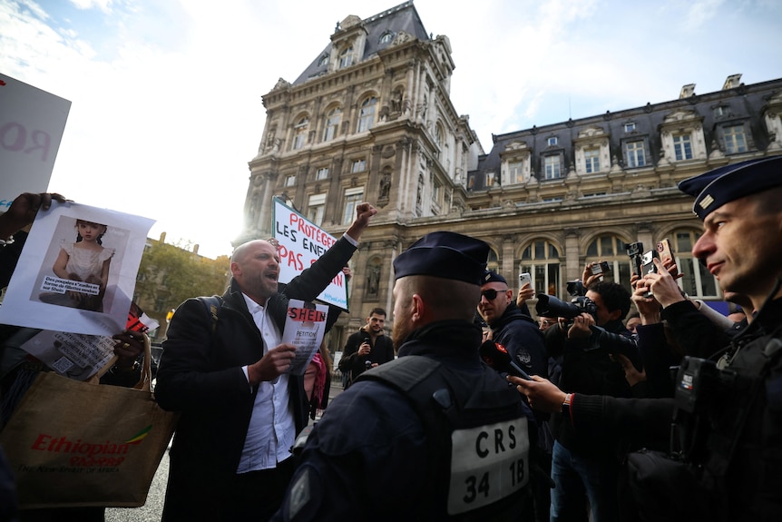 A group of people holding signs and protesting with police in front of them 