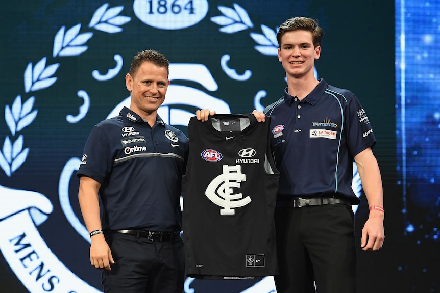Paddy Dow holds up a Carlton jersey with Brendon Bolton