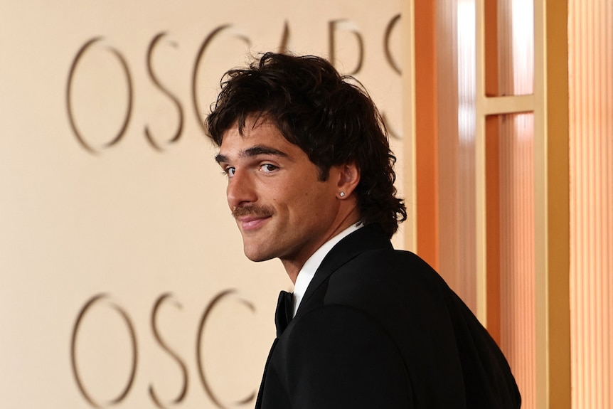 Jacob Elordi with head turned over the shoulder towards camera, dressed in formal clothes