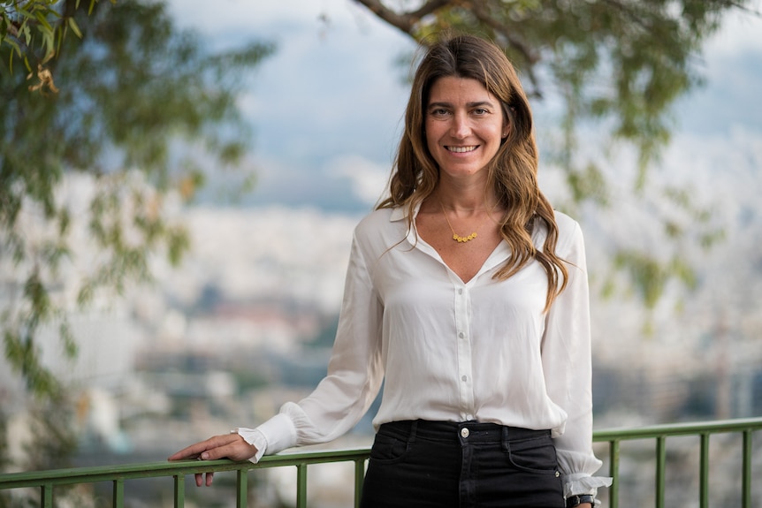 A young woman standing beside a railing above a view of a city.