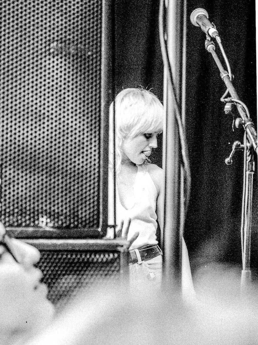 Black and white photo of woman standing back of music stage