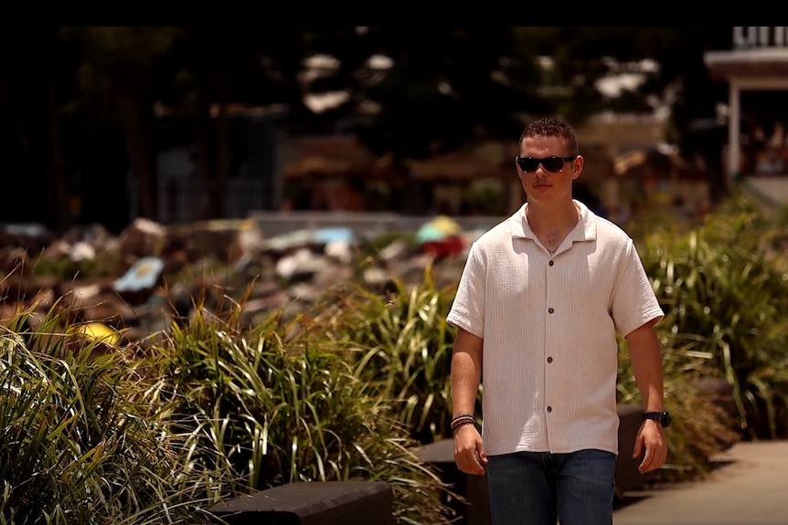 A young man walks next to the ocean.