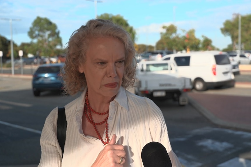 A woman in a white shirt speaks to a reporter