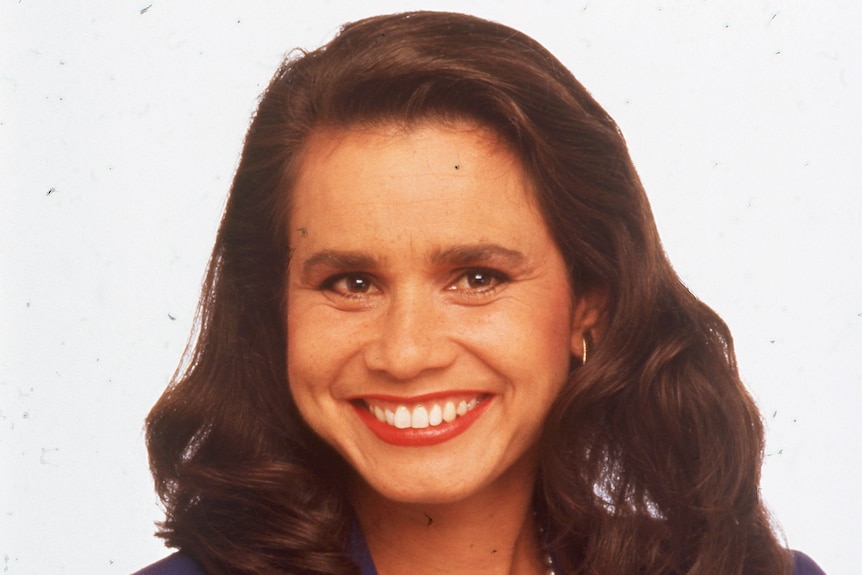 A young rhoda in a suit with her arms crossed. She smiles at the camera