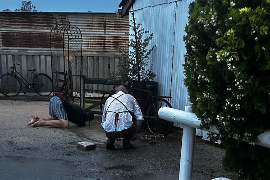 Two people crouching down at the base of a building, in flood water.