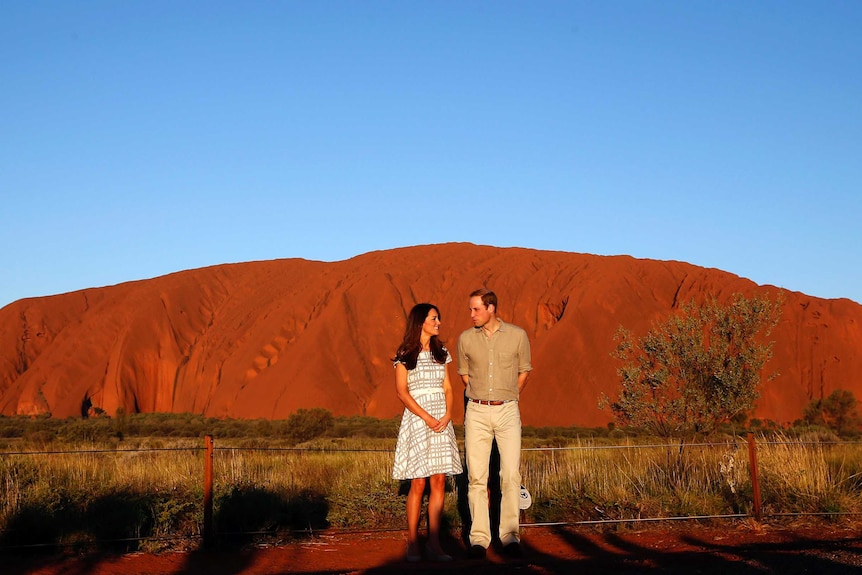 A smiling woman and man stand in front of Uluru.