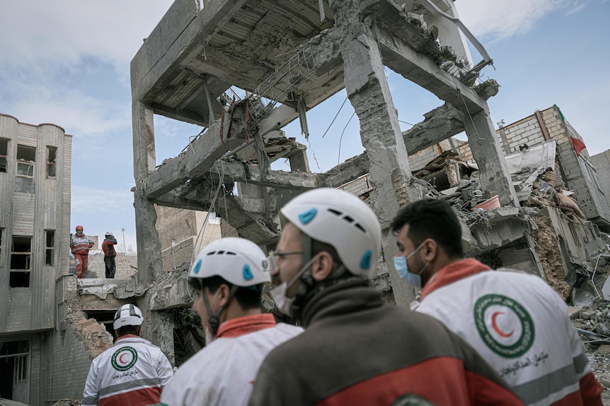 Men in white hard hats inspect a ruined tower.