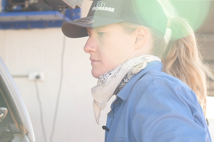 A young, blonde woman wearing a cap with her hair in a ponytail stands at the boot of a ute, as if she is packing it.