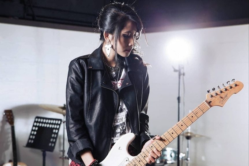A female with long black hair plays a guitar.
