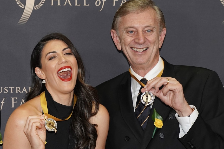 Dennis Cometti, pictured with swimmer Stephanie Rice, holds a medal and smiles. 