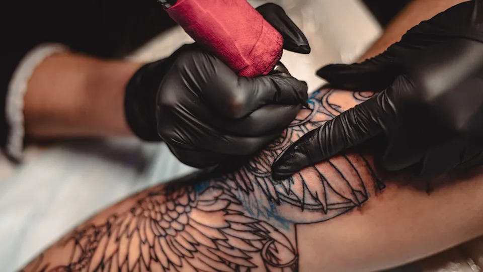 Professional tattoo artist makes a tattoo on a young man's leg