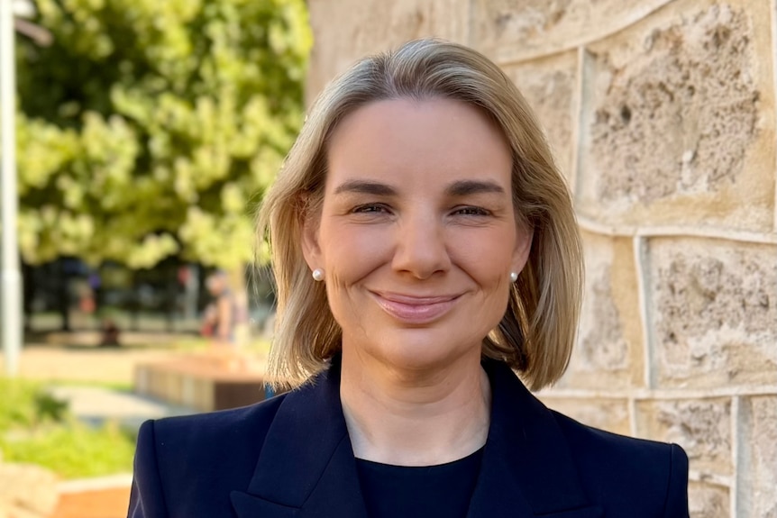 Jennifer in a suit, smiling, in a professional portrait outside of a building.