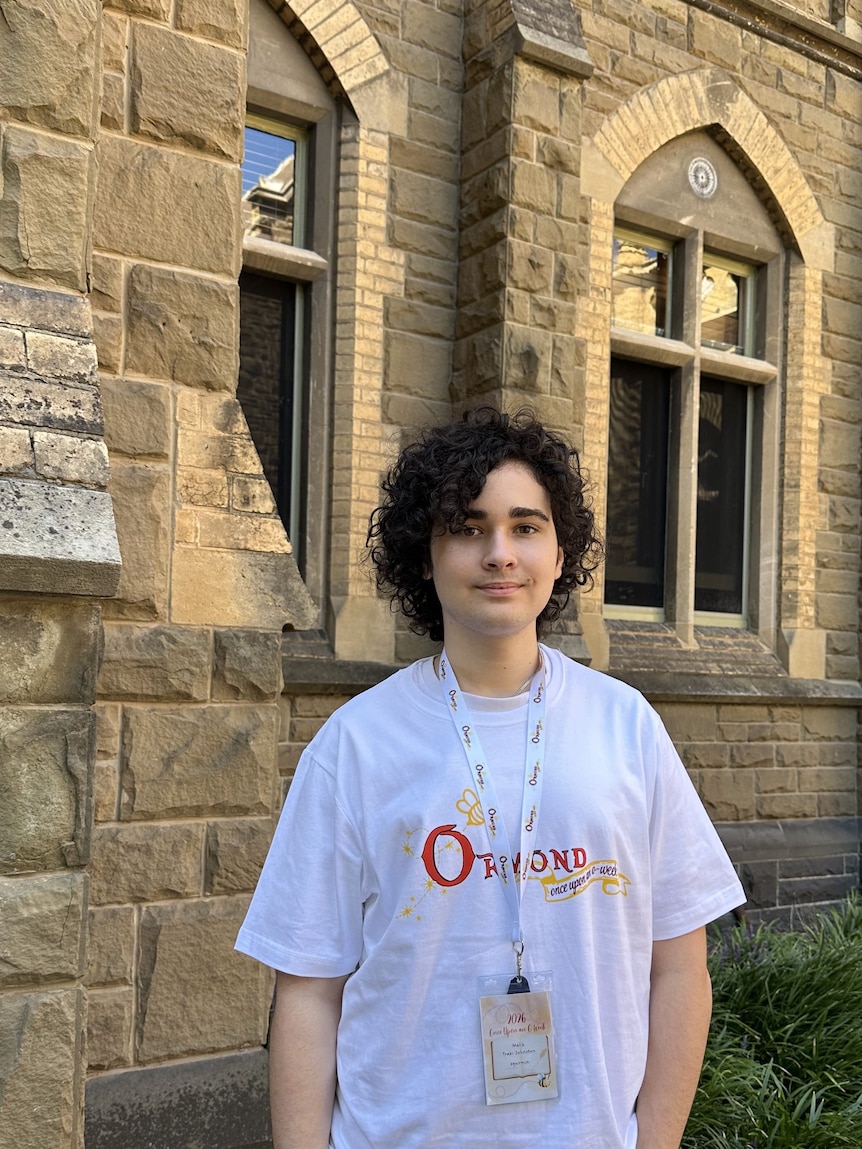 Malik stands in front of an old sandstone building wearing an Ormond college tshirt
