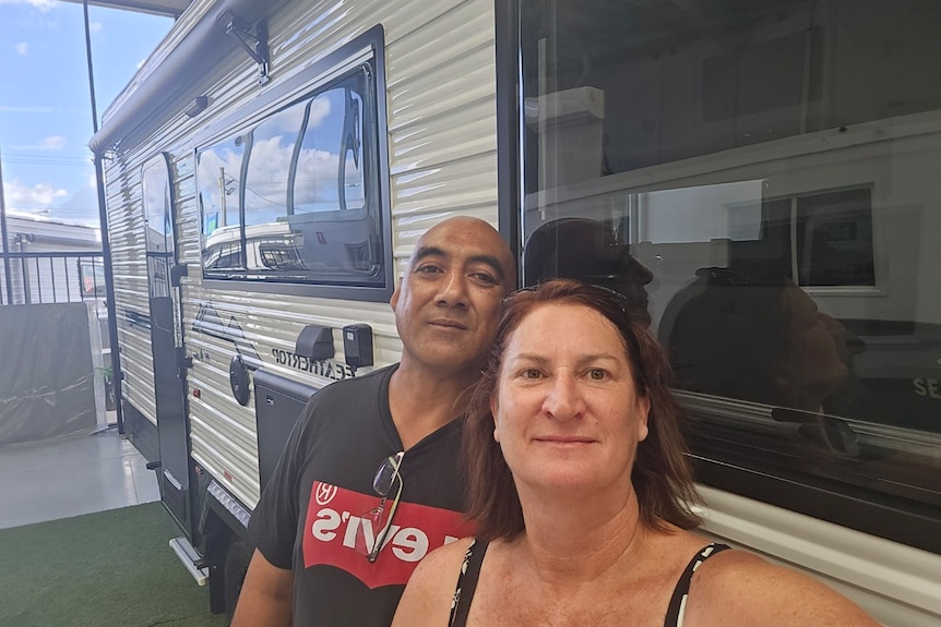 A man and woman stand in front of a campervan.