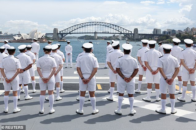 Sailors stand aboard HMAS Canberra, facing the Sydney Opera House and Harbour Bridge