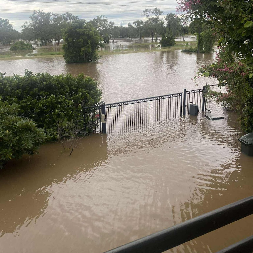 The view from a balcony, with brown floodwaters covering the residential street.