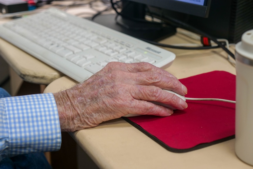 The hand of an elderly man holding a computer mouse.