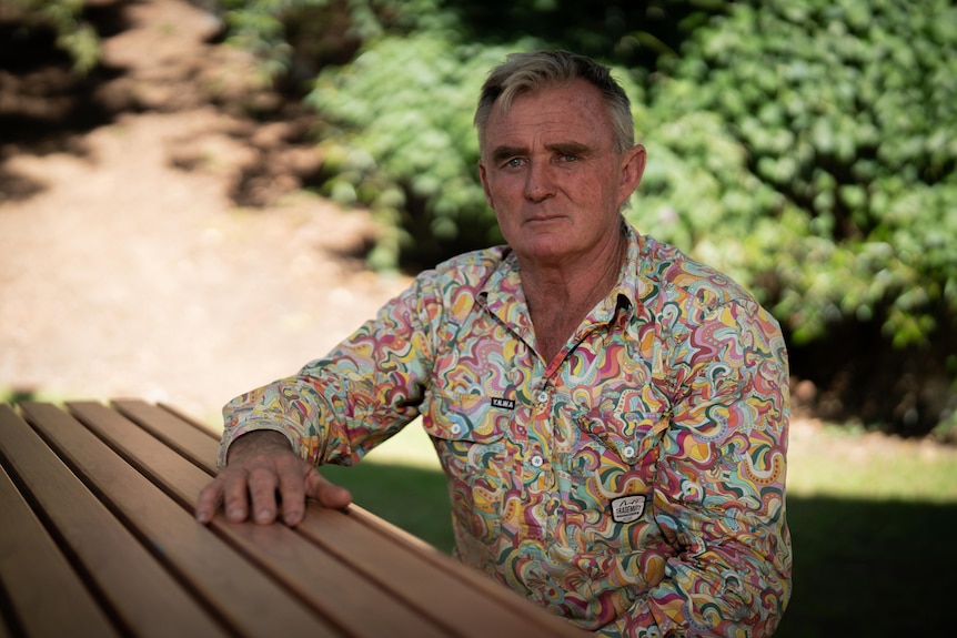 A man in a colourful shirt sits at a table.