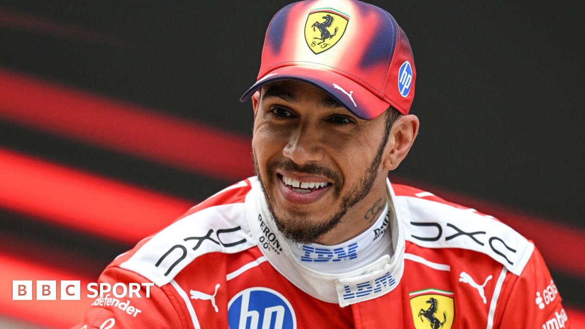 A smiling Lewis Hamilton wearing a Ferrari cap and race overall after he finished third in the Chinese Grand Prix