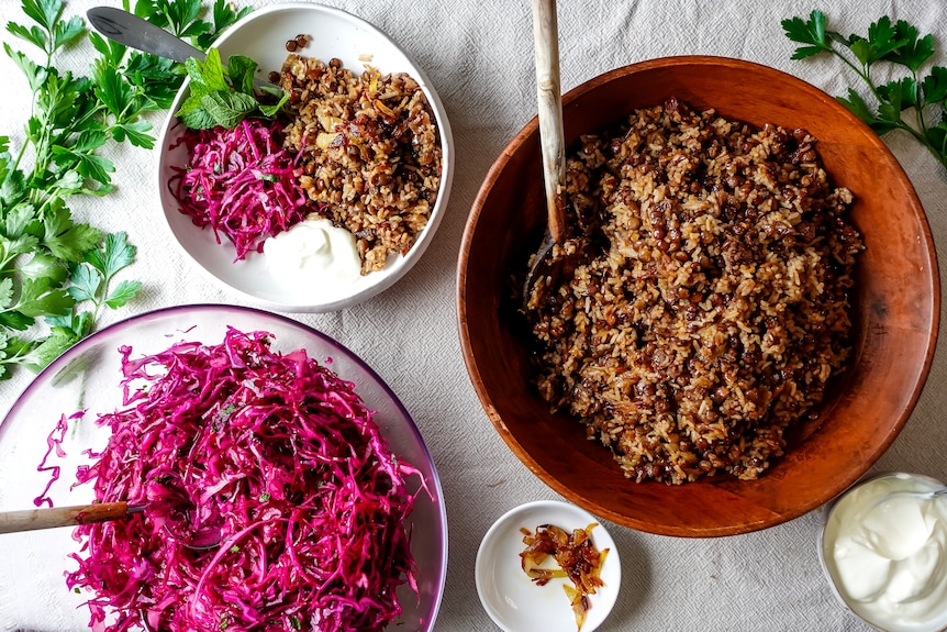 A large bowl of lentils and rice with caramelised onion alongside a bowl of sliced red cabbage and small bowl with both.