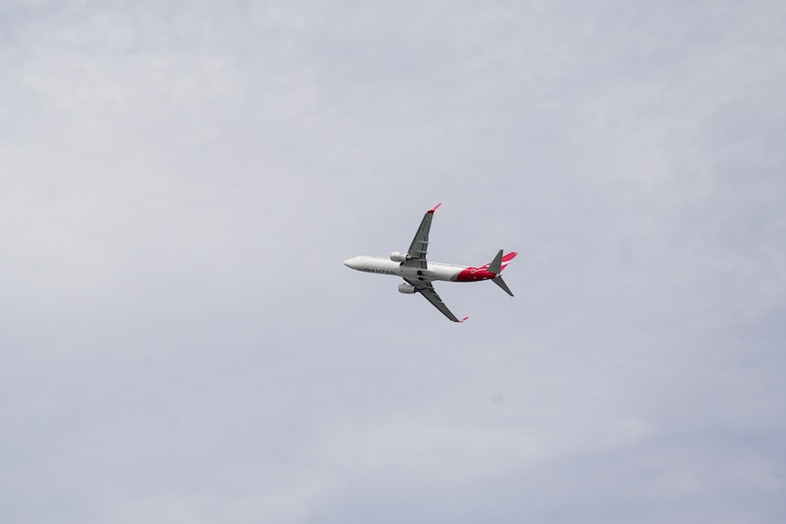 A Qantas plane can be seen in the sky leaving Sydney Airport.