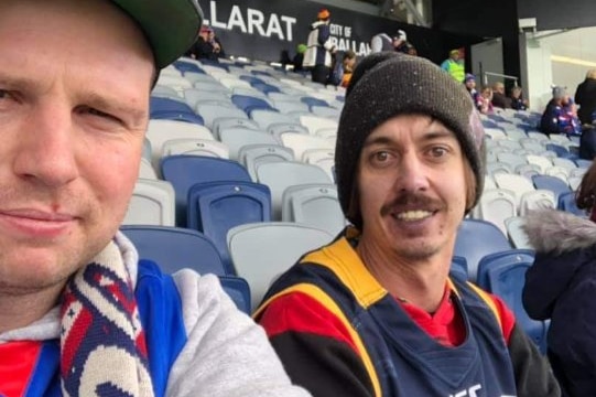 Two men sitting and watching a football game at the stadium. 
