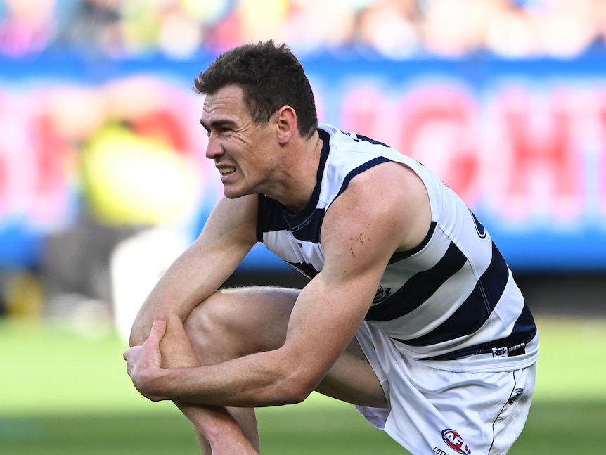 A Geelong forward crouches down on one knee and grimaces as he holds onto his right arm.