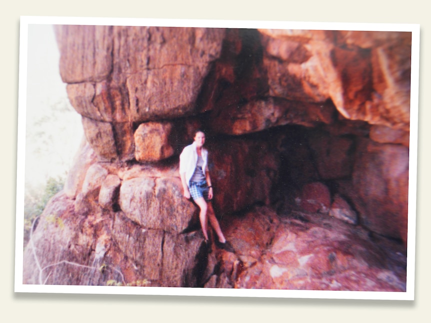 A young woman standing in front of a red rocky outcrop. 