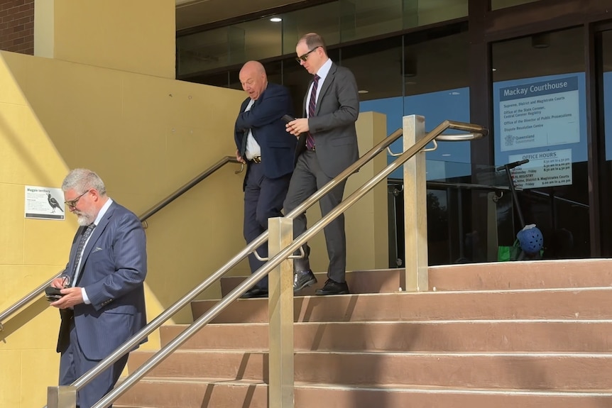 Three men in suits and ties walk down a flight of stairs in front of a court building.