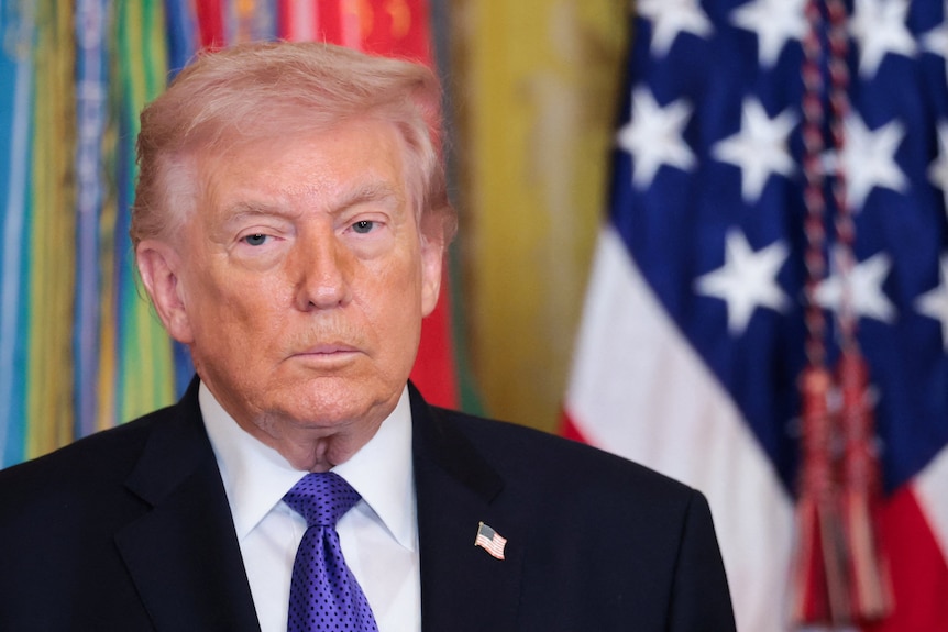 Donald Trump stands in front of a US flag.