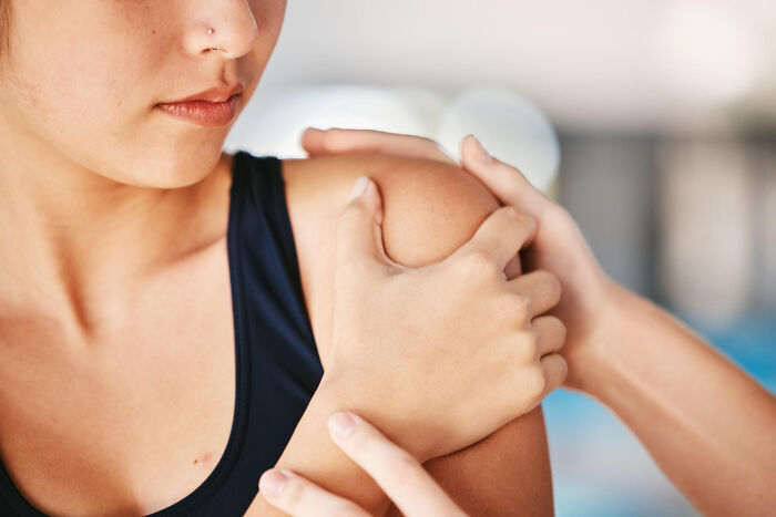 Close-up of woman in black tank top holding her shoulder, depicting a common case of patients faking pain symptoms.