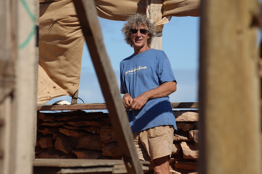 A man wearing blue t-shirt and sunglasses standing in damaged building.
